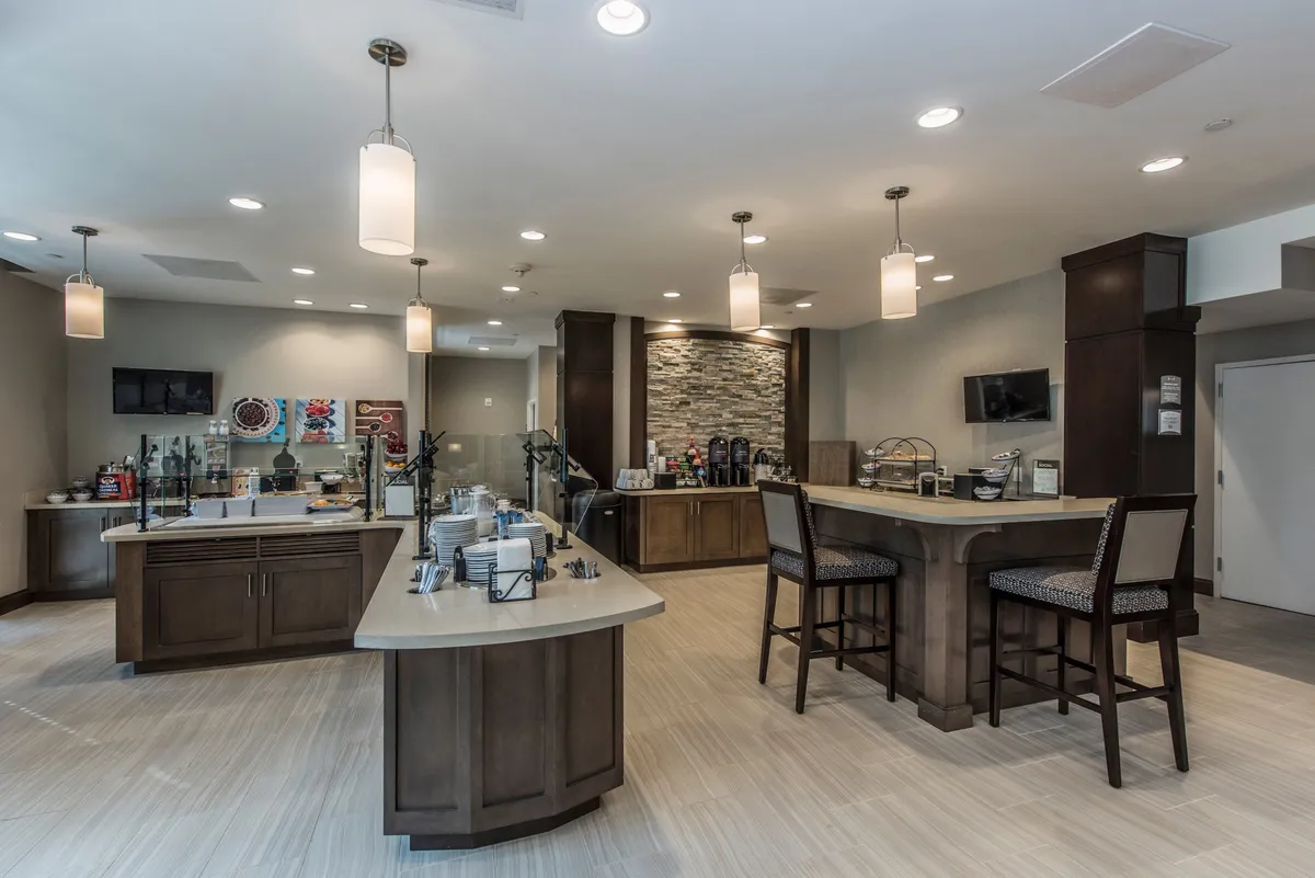 A bright and welcoming kitchen area centered around a central island with seating and a dedicated coffee station. The setting features stylish decor and artwork, suggesting a comfortable space for enjoying a morning brew or a casual meal.