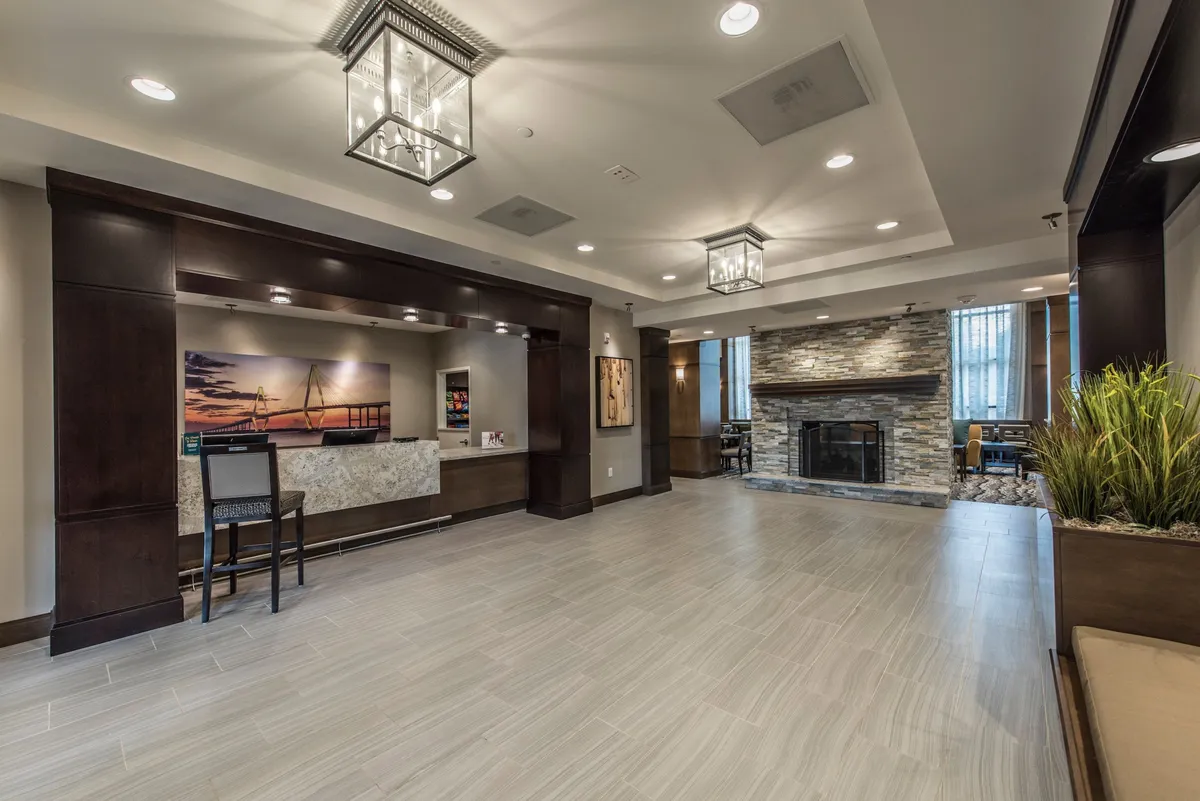 This inviting interior scene showcases the hotel reception desk with a glowing fireplace nearby, complemented by comfortable seating and elegant artwork. The space projects warmth and hospitality, suggesting a welcoming atmosphere for both leisure and business guests.