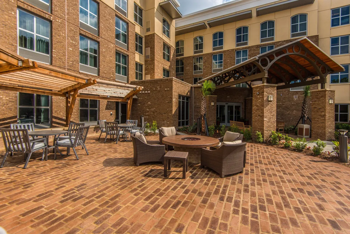 A welcoming exterior scene featuring a fire pit surrounded by comfortable seating, lush landscaping, and the building’s facade. It’s a cozy setting ideal for evening social gatherings and relaxed outdoor conversation.